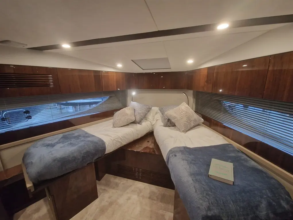 Brightly lit boat cabin with two single beds, decorative pillows, and a book on a blue throw. Modern, wooden finishes.